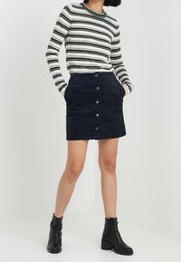 Randig långärmad topp i grön och vit, tillsammans med en marinblå kordkjol med framknappar. Svarta ankelstövlar fulländar looken.