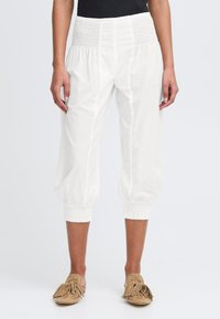 Pantalons blancs cropped avec une taille smockée, texture froncée et poignets élastiques. Le tissu semble léger et respirant.