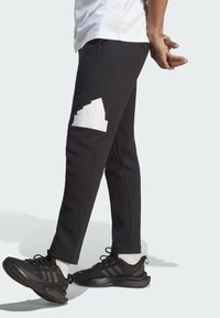 Svarta träningsbyxor i mjukt tyg, med en framträdande vit Adidas-logotyp på vänster lår och en smal, avsmalnande passform.