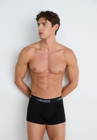 Schwarze Boxershorts aus glattem Baumwollmaterial, mit einem markierten schwarzen Gummibund mit weißer Schrift, getragen von einem männlichen Modell mit durchtrainiertem Körper.