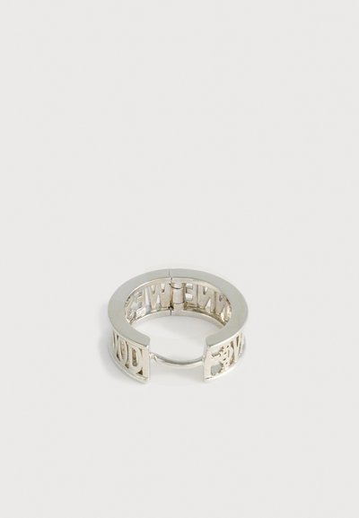 Anillo de plata con forma circular que presenta letras recortadas a lo largo de la banda. Textura suave con un acabado pulido y un cierre de bisagra.