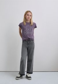 Tricou mov cu mâneci scurte, decorat cu un design cu craniu și oase încrucișate, asortat cu blugi largi gri cu pete de vopsea și adidași negri.