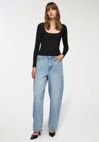 Czarna bluzka z długim rękawem o kwadratowym dekolcie i koronkowym wykończeniu, połączona z jasnoniebieskimi szerokimi spodniami dżinsowymi i czarnymi szpilkami z ostrym noskiem.