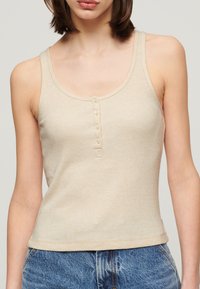 Beige ribbet tanktop med scoop halsudskæringer, der har fem knapper foran og en tætsiddende silhuet. Glat tekstur og ærmeløs design.
