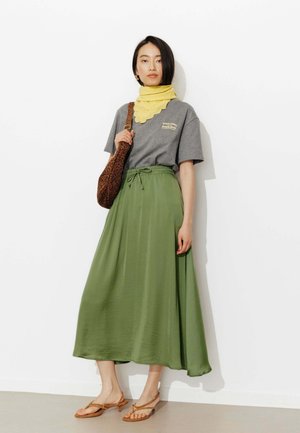 Femme portant une chemise grise à manches courtes, une écharpe jaune, une jupe midi verte, des sandales beiges et un sac à bandoulière marron à imprimé léopard.