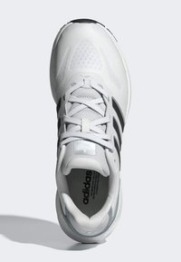 Zapatilla deportiva blanca con parte superior de malla, tres franjas negras, acentos texturizados y suela ligera. Presenta cordones blancos e plantilla con marca.
