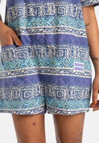 Short-sleeve patterned garment featuring blue and purple geometric designs, with a patch pocket and a branded label on the front.