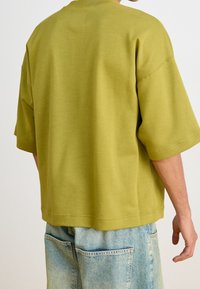 Överdimensionerad grön bomullströja med rund halsringning och korta ärmar. Baksidan har en slät yta och enkel sömmar.