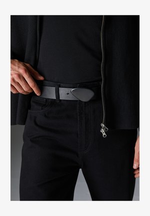 Juodas odinis diržas su dideliu trikampiu sagtimi. Dėvimas su juodomis kelnėmis ir tamsia palaidine, sukuriant monochrominį įvaizdį.