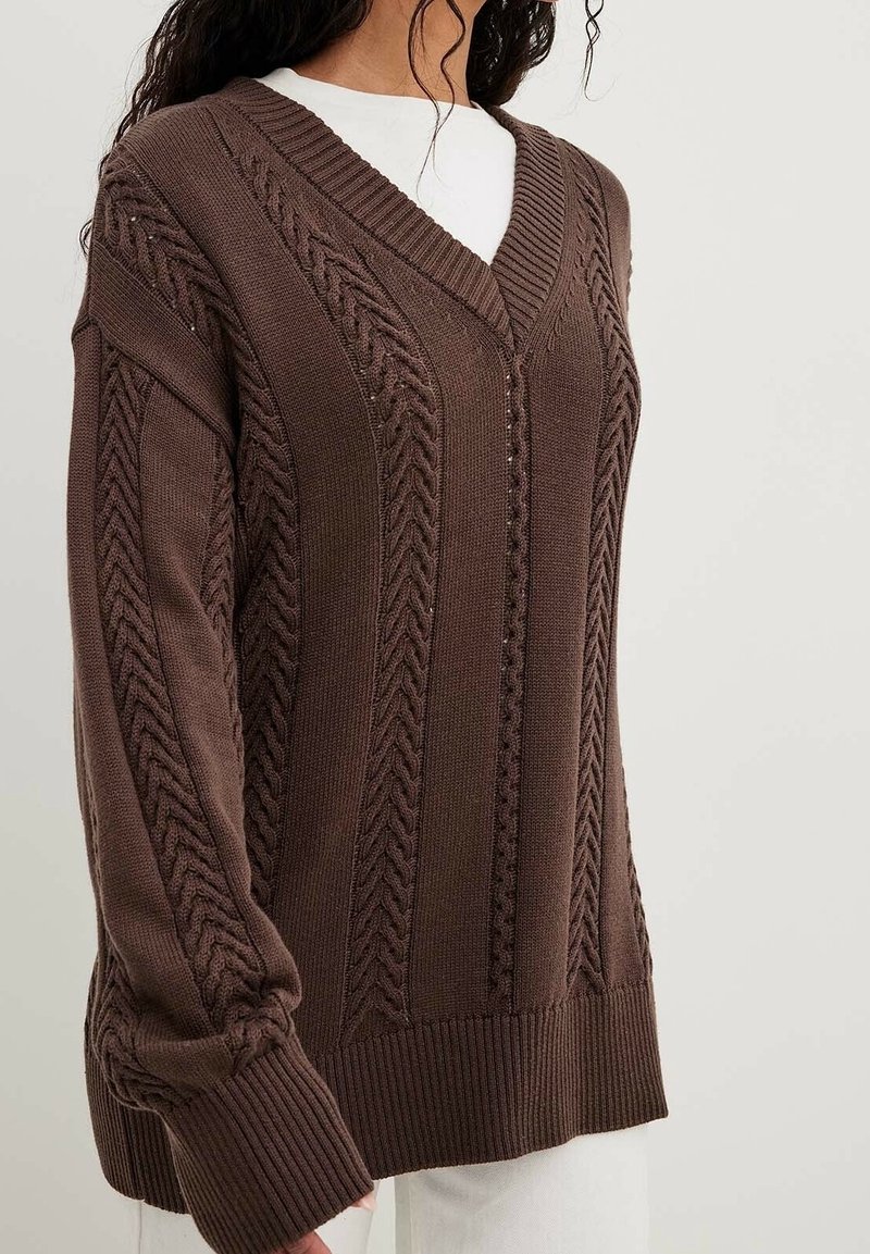 Brauner gestrickter Pullover mit V-Ausschnitt, der strukturierte Zopfmuster und gerippte Bündchen aufweist. Lockere Passform mit ausgeprägten Strickdetails.