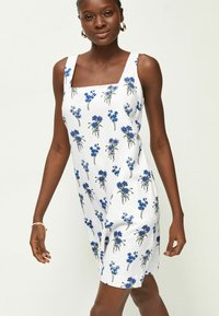 Blumenmusterkleid mit blauen Blumenmustern auf einem weißen Stoff. Mit quadratischem Ausschnitt und breiten Schulterträgern.