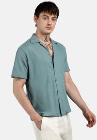 Camicia a maniche corte con bottoni in tessuto teal testurizzato, caratterizzata da un colletto alla francese, un motivo sottile e una vestibilità comoda.