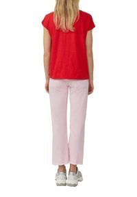 Haut rouge à manches courtes associé à un pantalon rose clair avec un ourlet effiloché. La tenue est complétée par des baskets grises et argentées.