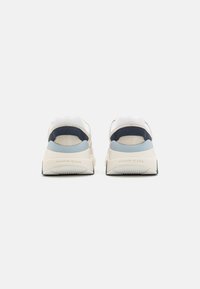 Zapatillas con una parte superior de malla blanca y acentos de gamuza, que cuentan con un talón azul oscuro, suela con marca y una mediado gruesa blanca para soporte.
