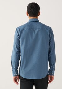 Chemise bleue à manches longues en tissu texturé, dotée d'un empiècement au dos et de poignets boutonnés. Coupe ajustée avec un ourlet arrondi.