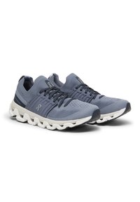 Leichte Sportschuhe aus grauem Mesh-Material mit gepolstertem Kragen, schwarzen Schnürsenkeln und weißem Dämpfungssohle mit abgerundeten Akzenten.