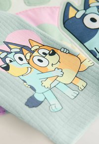 Weiche Baumwolldecke mit verspielten Cartoon-Tieren in sanften Farben. Blaue und orange Hunde umarmen sich vor einem hellgrünen strukturierten Hintergrund.