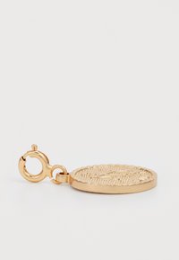 Charm en métal doré de forme circulaire, avec une surface texturée et des détails gravés. Comprend un fermoir pour fixation.