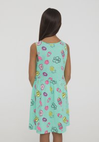 Un vestito azzurro chiaro con un divertente motivo di gelati, ciambelle, fiori e fenicotteri nei colori rosa, giallo e nero. Maniche a spalla.