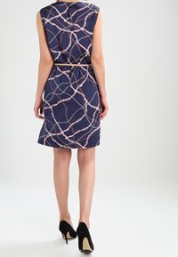 Vestido sin mangas azul marino con un patrón de eslabones en rosa y plata. Presenta una cintura con cinturón y un corte recto. Combinado con tacones negros.