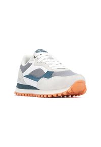 Zapatilla gris y blanca con parte superior de malla y ante, acentos en color azul verdoso y suela de goma naranja. Presenta cordones y un collar acolchado.