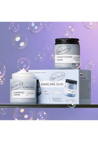 Set duo per la cura dei capelli con un barattolo bianco di crema shampoo e un barattolo di crema balsamo con coperchio nero, posizionati su uno sfondo viola con bolle.
