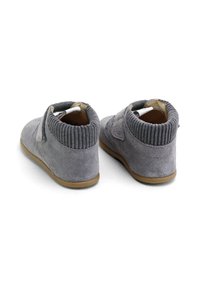 Botas de tobillo de ante gris con cuello de punto acanalado, suela de goma plana de color marrón y cinturón de velcro en el lado. Textura suave y diseño redondeado.