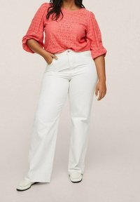 Haut corail à manches courtes avec un motif texturé, associé à un jean blanc taille haute à jambe large et des chaussures légères à enfiler.