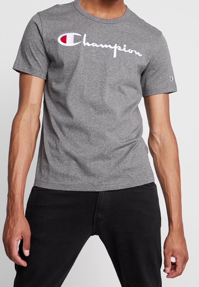 Maglietta in cotone grigia con un evidente logo bianco "Champion", maniche corte e scollo classico a girocollo.