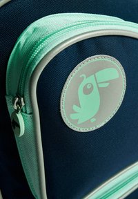 Mörkblå ryggsäck med dragkedja och detaljer i mintgrön. Har en cirkulär logotyp av en stiliserad fågel i mintgrön. Texturerat tyg.