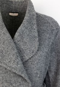 Pilkas vilnos mišinys paltas, turintis iškeltą apykaklę, grublėto audinio su zigzago raštu ir švarių siūlių detalėmis.