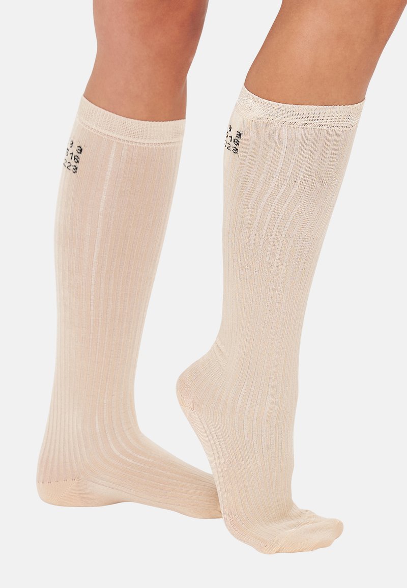 Chaussettes beiges montantes avec une texture côtelée et un renfort au niveau des orteils. Présente des chiffres noirs imprimés sur le bandeau supérieur. Tissu doux et extensible.