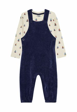 Mørkeblå corduroy overalls med justerbare stropper, knapper i siden og elastiske manchetter, lagd ovenpå en cremefarvet bluse med lange ærmer og sejlbådsmønster.