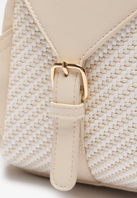 Beige kézitáska szőtt mintával, sima bőrrel, aranyszínű fémrészekkel, állítható pánttal és lapos csattal.