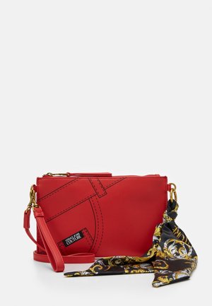 Petite pochette en cuir rouge avec une écharpe noire et dorée à motifs attachée à la quincaillerie dorée, décorée de surpiqûres imitation jean et de l'étiquette Versace Jeans Couture.