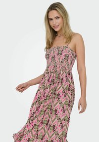 Bröstlös maxiklänning i rosa, grön och brun mönstrad tyg. Har en smocksömnad bodice och ett flödande kjol. Mjukt, lätt material.
