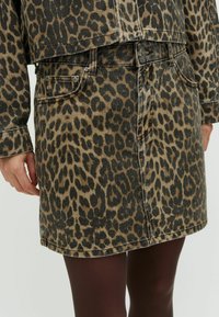 Fustă din denim cu un model de leopard, având talie medie, buzunare frontale și o siluetă dreaptă. Culorile includ nuanțe de maro și negru.