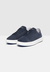 Sneaker in suede blu navy con suole in gomma bianche, caratterizzate da dettagli perforati e una finitura liscia sulla parte superiore. Lacci per una vestibilità sicura.
