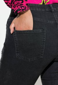 Jeans de denim negro con un diseño ajustado, que cuentan con un bolsillo trasero y un ligero desgaste. El material tiene una textura suave y resistente.