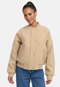 Sweatshirt beige avec un col rond, fermeture à boutons et poignets côtelés. Dispose de poches latérales et d'un tissu doux et texturé.