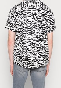 La camicia a maniche corte presenta un motivo a strisce tigre bianco e nero, realizzata in tessuto leggero, con orlo dritto e vestibilità rilassata.