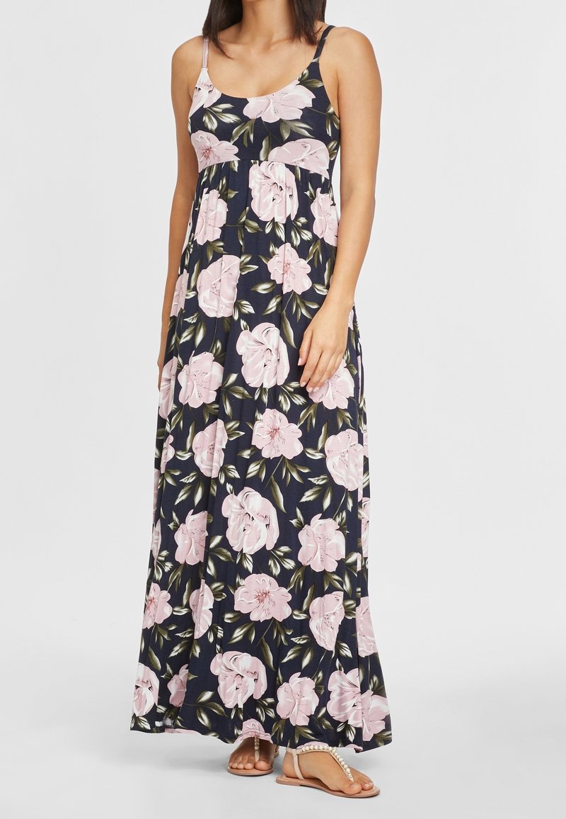 Kwiecista sukienka maxi na cienkich ramiączkach, granatowe tło, jasnoróżowe kwiaty, zgromadzony biust, luźny krój, zestawiona z prostymi sandałami.