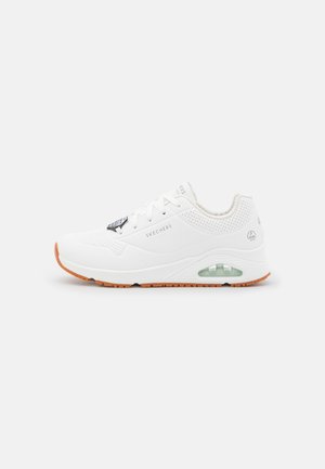 Weißer Sportschuh mit perforierten Details, Schnürverschluss, sichtbarem Luftdämpfungselement und orangefarbener Gummisohle. Markenlogo an der Seite.