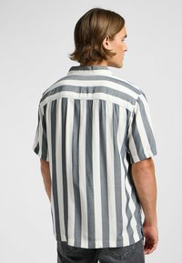 Chemise à manches courtes avec des rayures verticales grises et blanches, une texture douce, un col à boutons et un design à dos plissé.