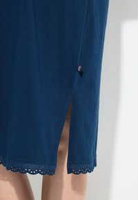 Granatowa sukienka z miękkiego materiału, z boku rozcięciem i falbaniastym dołem z perforowanymi detalami. Metka w kolorze czarno-białym.