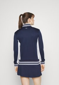 Navy blue athletic dress with a high collar, white side panels, and striped accents. The fabric is smooth with a slightly stretchy texture.