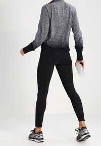 Zwarte sportlegging met een aansluitend ontwerp, gecombineerd met een donkergrijze trui met een textuurpatroon en zijsplitten, gedragen met hardloopschoenen.