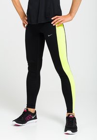 Leggings sportivi neri con un pannello laterale giallo neon. Realizzati in materiale elastico, presentano un design aderente e un logo Nike sul fianco.