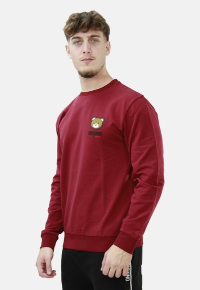 Felpa color amaranto realizzata in morbido tessuto con una grafica di un orso sul petto. Le maniche lunghe e i polsini a costine aumentano il comfort.