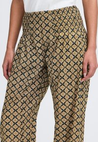 Gemusterte Weite-Hosen mit schwarzem Grundton, goldenen und cremefarbenen geometrischen Motiven, gerafftem Taillenbund und weichem Stoff. 